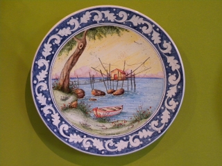 (CODICE ARTICOLO: HI/21) Piatto in ceramica, dipinto a mano, raffigurante il trabocco e cornice classica blu e bianca. tecnica: maiolica